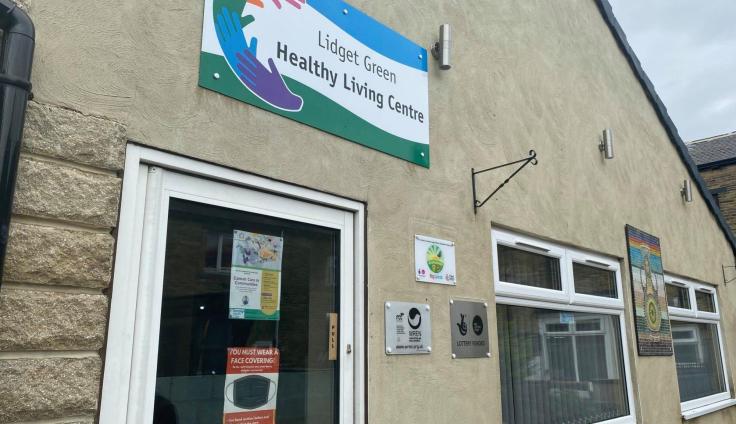 The front of a building with a door and window and a colourful sign saying 'Lidget Green Healthy Living Centre.'