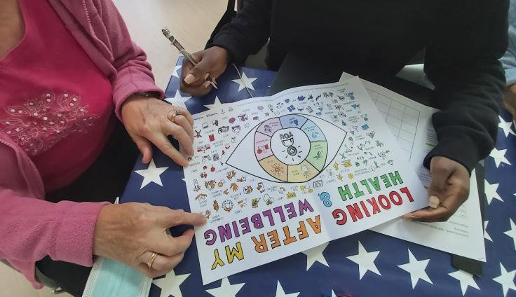 An overhead view of two people looking at a piece of paper which reads 'Looking after my health and wellbeing'.