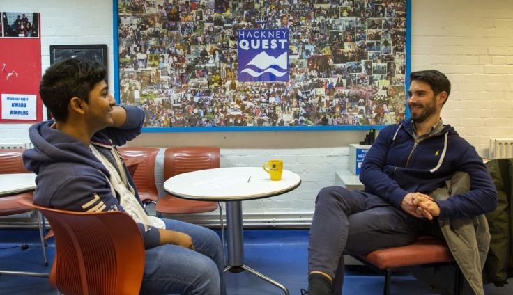 Two young men sitting on chairs and chatting across a table.