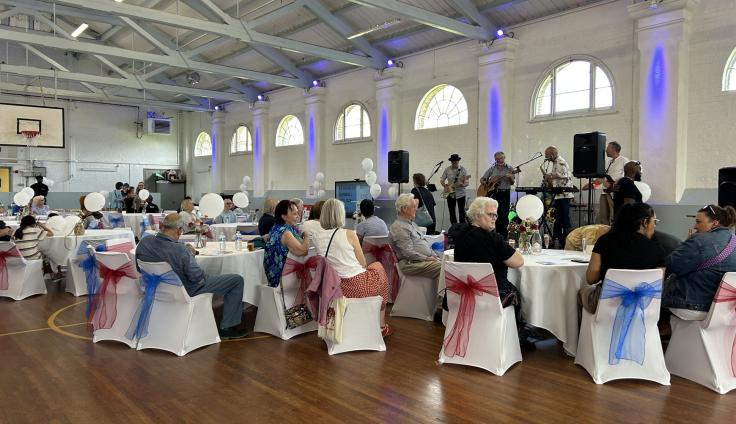 People seated on chairs around decorated tables, with a band playing in the background.