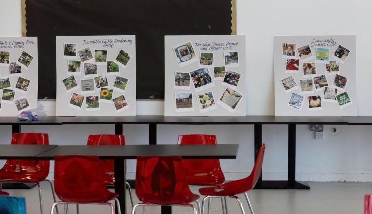 Display boards featuring photosgraphs and texts, resting on tables in a room with bright red chairs.