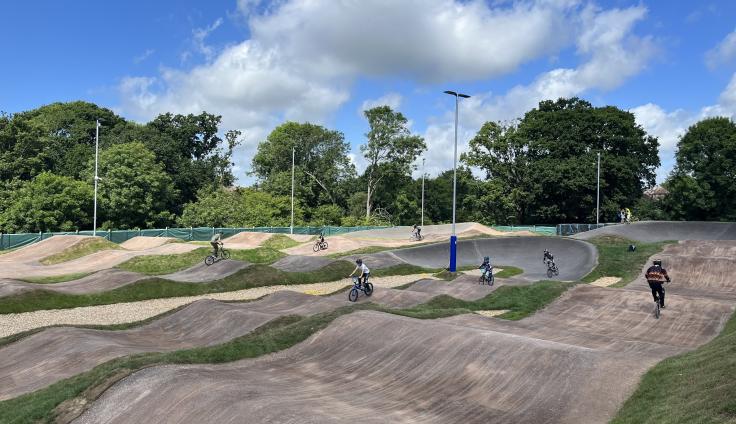 An undulating concrete bike track set in a parkland area, with trees in the background.