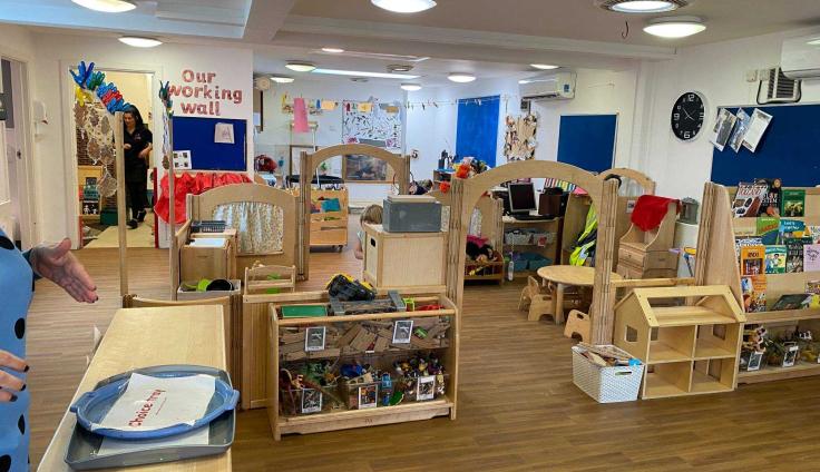Wooden desks, archways and table and chairs inside a room with blue noticeboards on the wall.