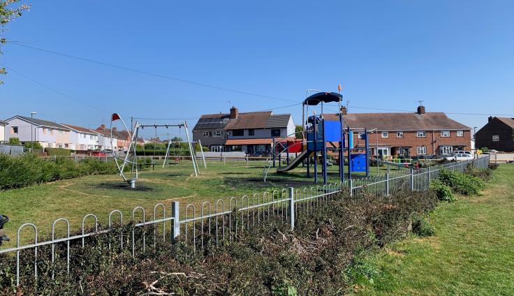 A grassy play area behind railings with a climbing frame and swings.