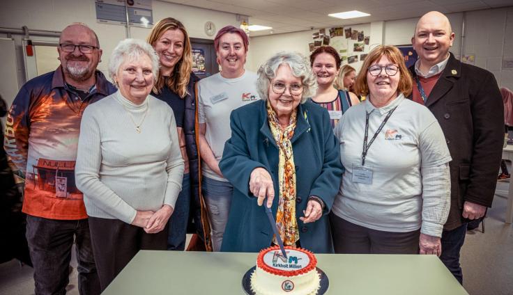 A group of people smiling at the camera, with one person cutting into a cake.