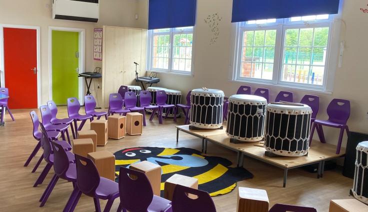 Purple chairs placed in a semicircle around a small stage with 3 large drums inside a school hall