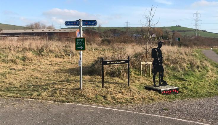 A silhouette style statue of a soldier on the crossroads of a pavement and a footpath.