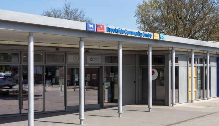 A modern single-storey building with glass windows, with a sign reading "Brookside Community Hub" above the frontage.