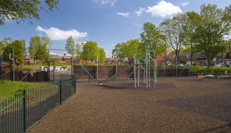 A tidy play area with grassy areas and trees in the background.