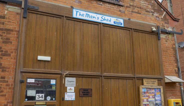 Large wooden doors to a red-brick building with a sign reading 'The men's shed'.
