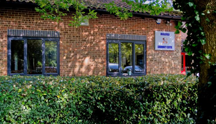 Two windows of a red-brick single-storey building with a hedge in front.