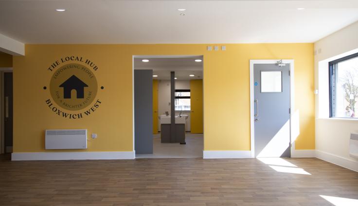 A large yellow room with wooden flooring, with sun streaming in and a mural reading 'The Local Hub' on the wall.