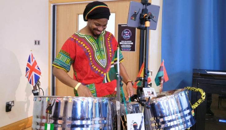A smiling man playing steel drums, wearing a colourful outfit.