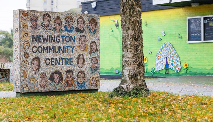 A mosaic sign reading 'Newington Community Centre' standing outside a single-story building with a colourful mural on the side.