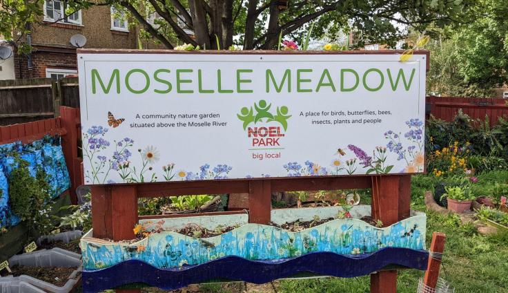 A sign reading 'Moselle Meadow' in a green space with trees and plants.