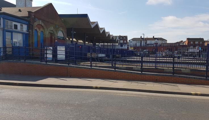 Train station with a long paved ramp with railing, and parking lot in the background.
