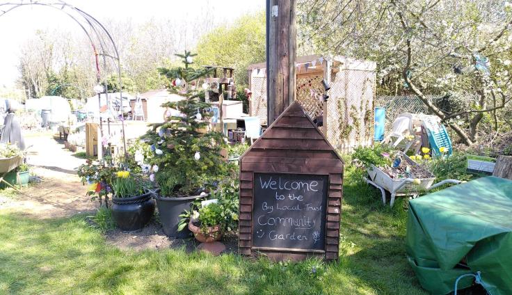 A garden with grass, plants and trees and a chalkboard sign reading 'Welcome'.