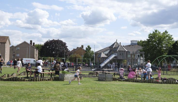 Children playing in the play and picnic area on Tantony Green. The play area sits in the middle of a grassy area. Houses and trees can be seen in the background.