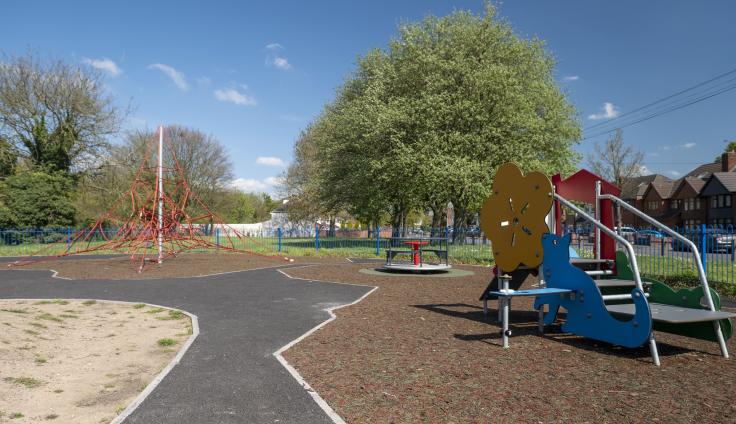 Play equipment including a slide in a sunny playground with trees.