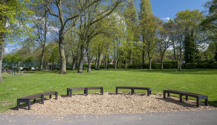 A circular seating area in front of a grassed area surrounded by trees.