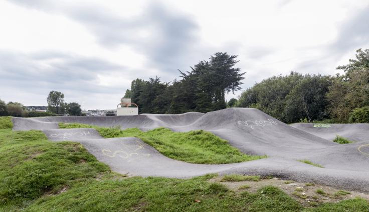 A paved track for BMX bikes, set within green space with trees in the background.