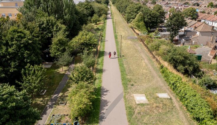 An aerial shot showing people walking along a raised pathway between housing surrounded by trees and grassy areas.