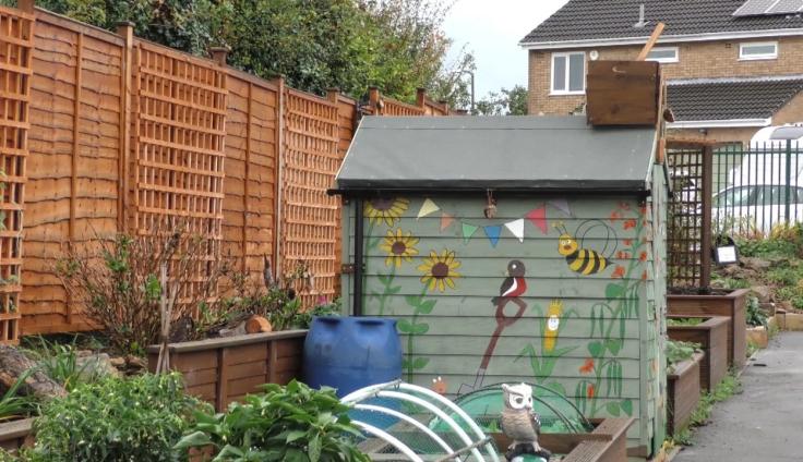 A garden shed with a bright mural and raised beds.