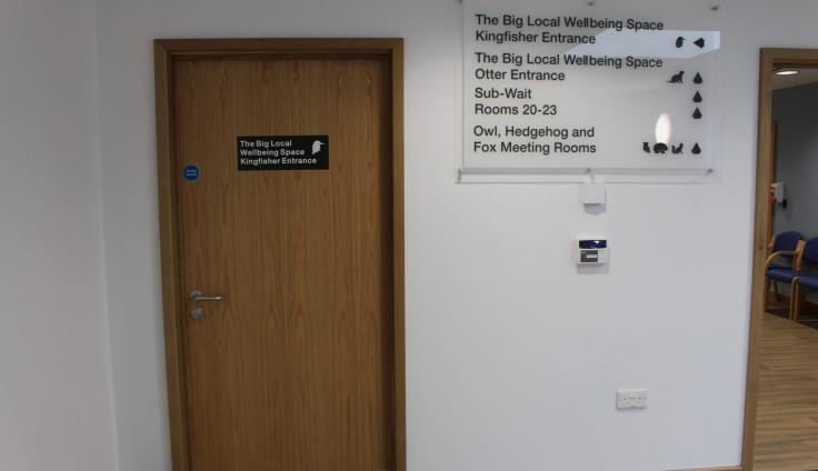 A wooden door with signs pointing to surgery facilities including a wellbeing area.