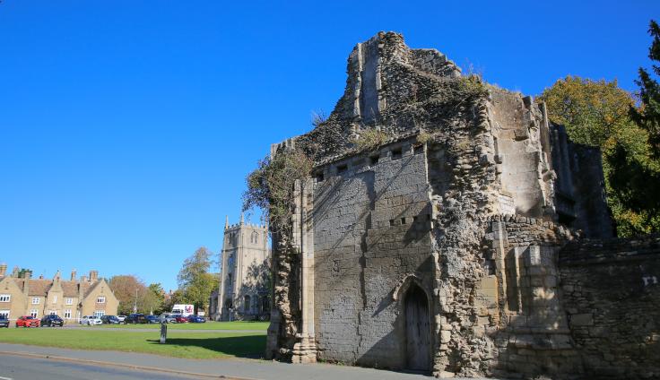 Exposed stone building with a church tower and green space in the background