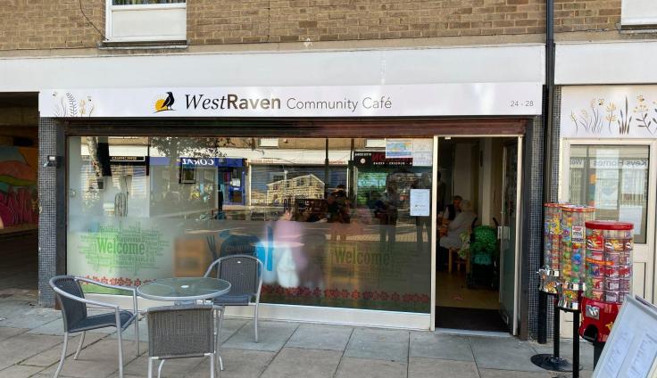 Large window front of WestRaven Community Café with table and chairs outside.
