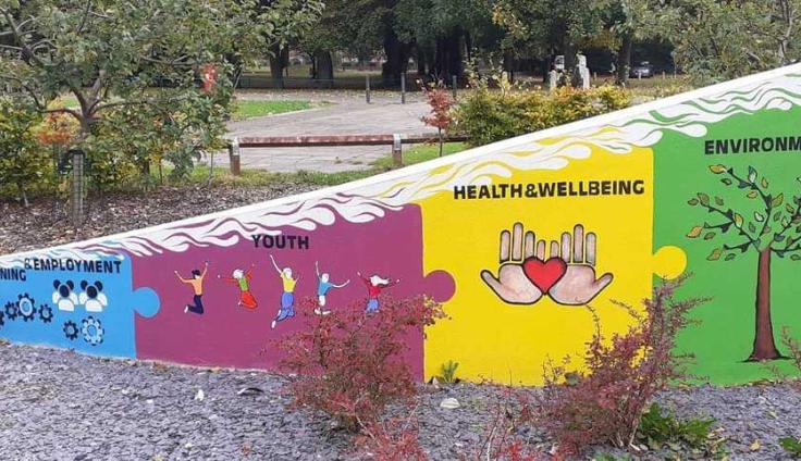 A colourful mural on a garden wall with painted words including 'environment' and 'health and wellbeing,'
