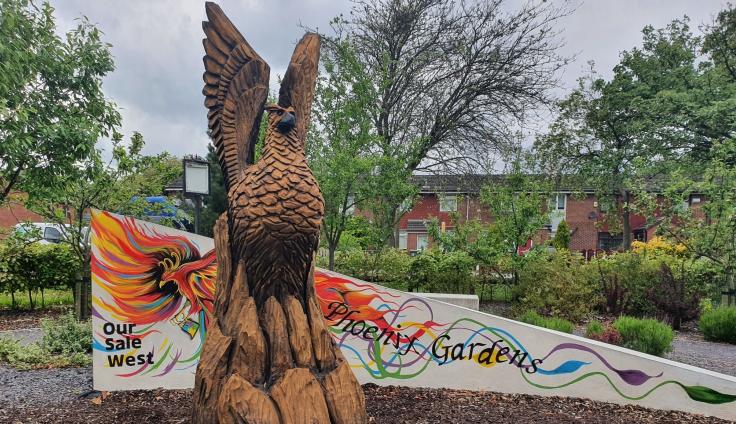 A carved wooden phoenix in a park setting.