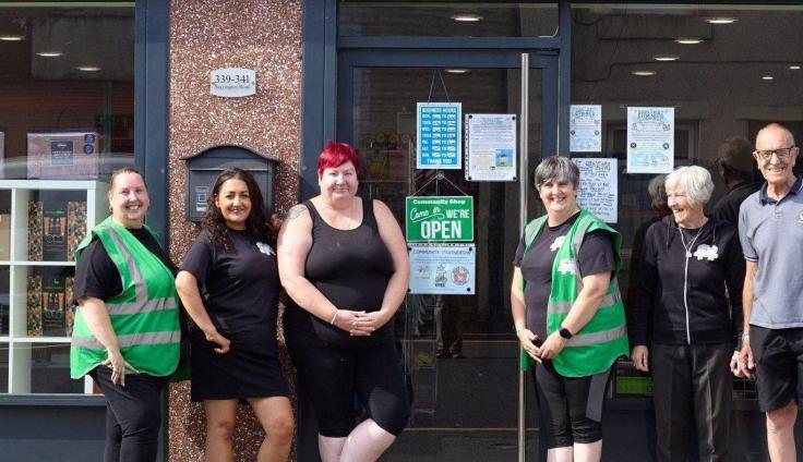 Six members of the team standing in front of The Big Local Community Shop storefront, underneath the large storefront sign.