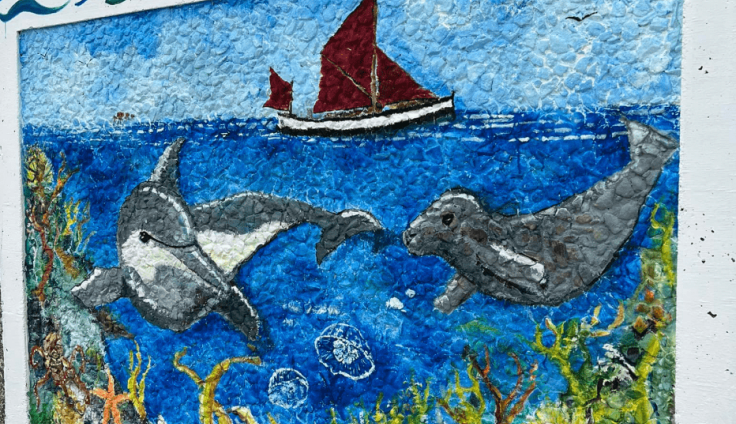 A colourful mural of a dolphin and a seal below water with a red sailboat above.