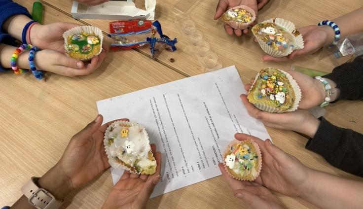Looking down onto a people's hands on a table, with each person holding out a small iced cake.