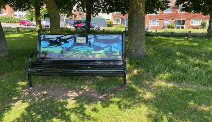 A decorated bench in a grassy area, under the shade of trees.