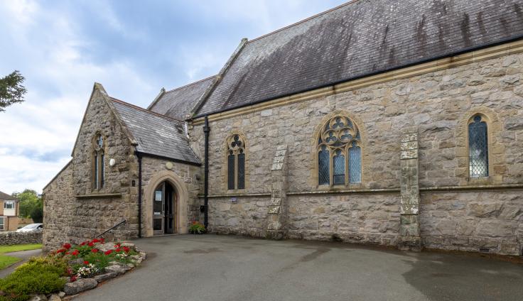 A grey stoned church building with a colourful flowerbed
