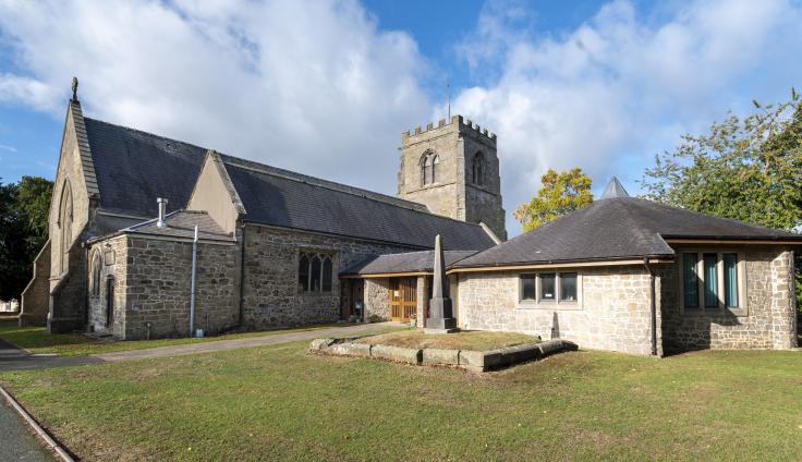 A grey stoned church and one-storey annexe with green space outside