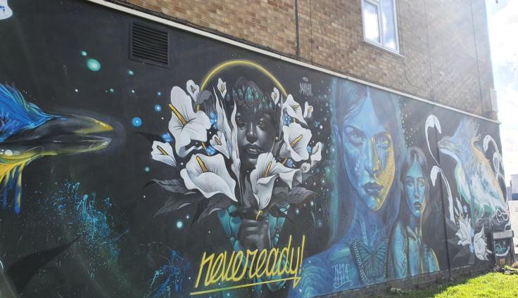 A mural on a wall with flowers and people's faces in blue and white shades.