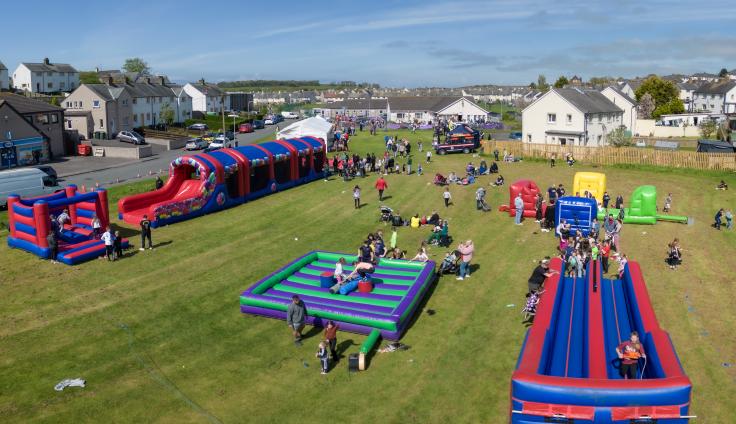 Aerial shot on a sunny day of a field surrounded by houses, with large colourful bouncy castles and people bustling about.