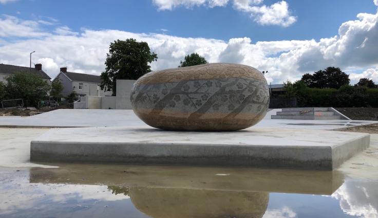A view of the community plaza, with a large boulder in the foreground, engraved with blossom tree patterns.