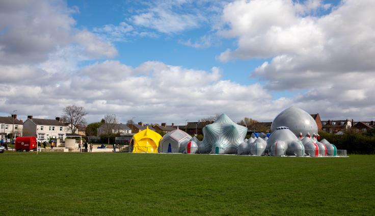 Large green space with grey inflatable sculpture in the background