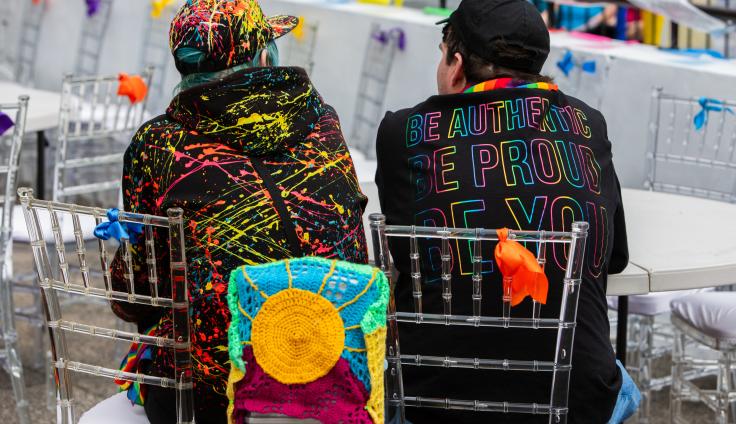 Two young people sitting down, facing away from the camera, with black jumpers and colourful patterns on them.