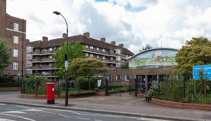 A red-brick housing block with a mural over a building and a red post box near a road junction.
