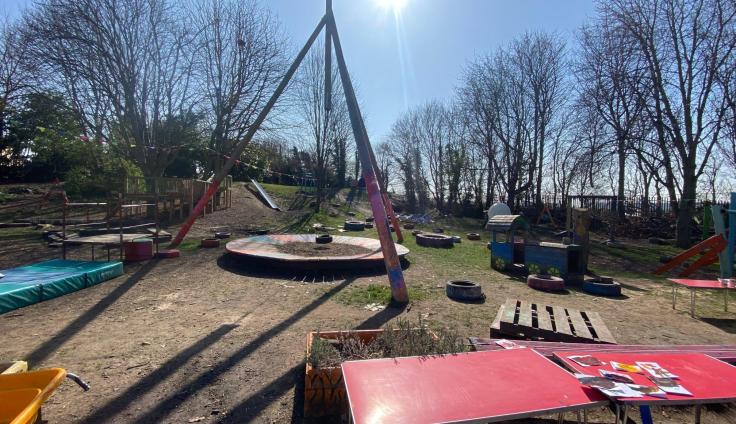 Play equipment including a large wooden swing in the sunshine.