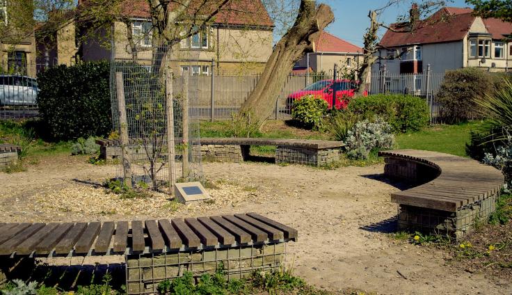 Wooden slatted seating in a circle around a tree, surrounded by grassy areas.