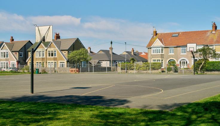 A basketball court in front of 1930s semi-detached houses.