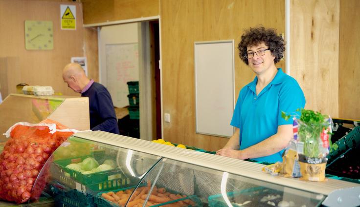 Two people standing behind a food counter, full of fresh vegetables.