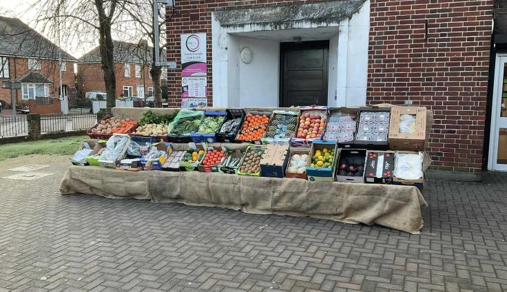 A well-stocked fruit and vegetable stall in front of a red-brick building.