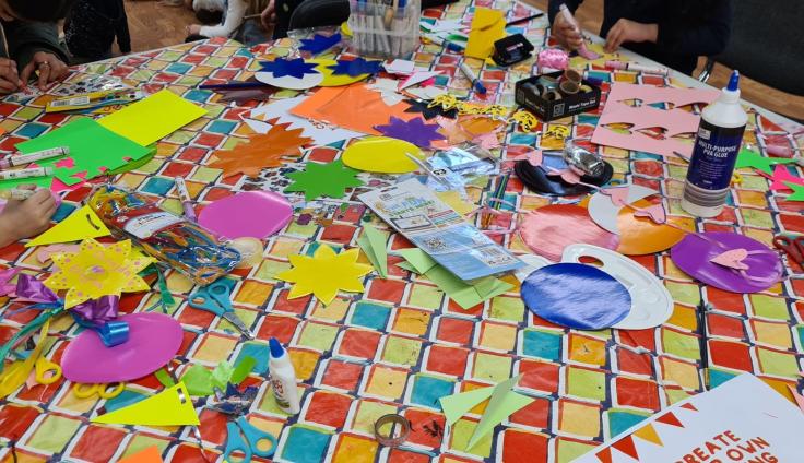 Small hands doing activities on a table covered with brightly coloured crafting items.